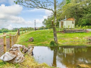 A rustic cabin with a wooden deck, surrounded by a fenced garden and a small pond. - 1 Bed in Pembroke (oc-89099) (Lamphey)