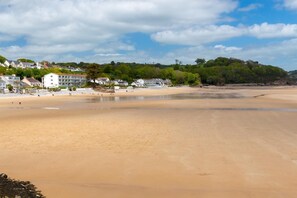 A wide sandy beach with a few buildings in the background. - 1 Bed in Pembroke (oc-89099) (Lamphey)
