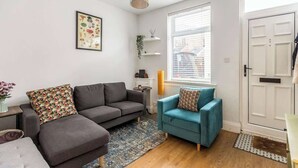 Un salon avec un canapé gris, un fauteuil turquoise, un tapis à motifs, un tableau accroché au mur et une porte blanche.