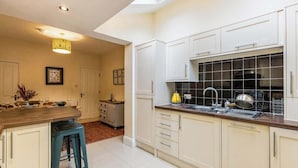 Une cuisine avec des meubles blancs, un îlot central doté de tabourets, un pare-feu en carreaux noirs et un éclairage encastré au plafond.