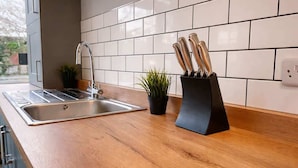 Uma cozinha com pia de aço inoxidável, bancada de madeira, plantas em vasos e porta-facas.
