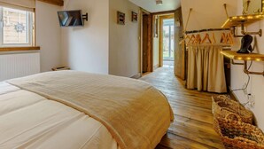 Ein Schlafzimmer mit einem Bett, einem Fernseher, Holzboden, einem Flur und einem Badezimmer mit Handtuchhalter.
