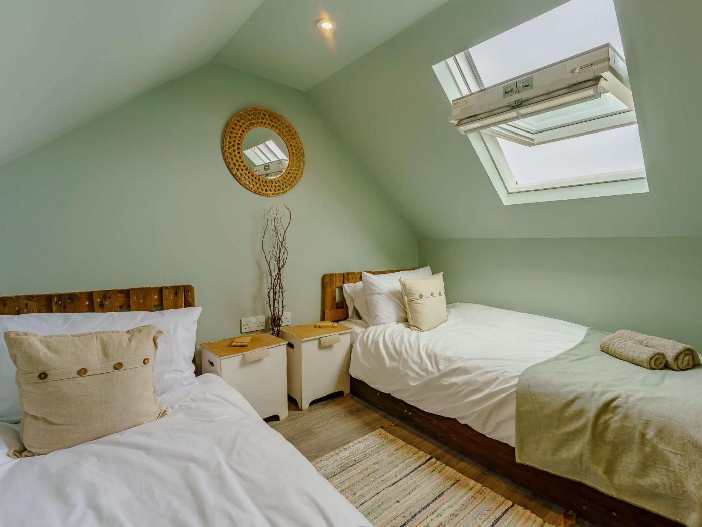 Quarto com duas camas, um claraboia, ar condicionado fixado na parede e um espelho decorativo.