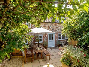 A stone house with a patio, a table with chairs, and an umbrella. - 2 Bed in Fakenham (oc-89014) (North Creake)