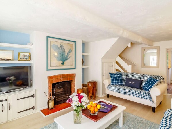 A living room with a fireplace, a sofa, a coffee table with flowers and fruit, and a staircase. - 2 Bed in Fakenham (oc-89014) (North Creake)
