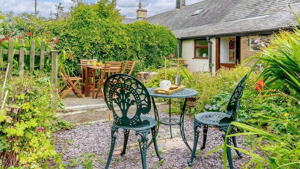 Ein rustikales Cottage mit Garten-Terrasse, einem Holztisch und Metallstühlen.