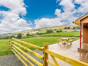 A wooden deck with picnic tables overlooking a green field and hills.