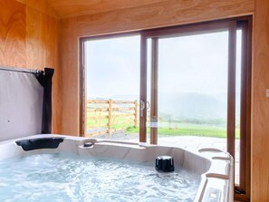 A wooden cabin with a hot tub, large sliding glass doors, and a view of a grassy area. - 2 Bed in Llandrindod Wells (oc-89063) (Nantmel)