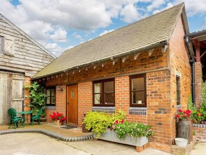 A brick building with a gabled roof, a wooden door, and a small porch with green chairs and potted plants. - 1 Bed in Shrewsbury (oc-89144) (Leighton)