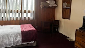 Una habitación con cama, una silla, cómoda y televisor.