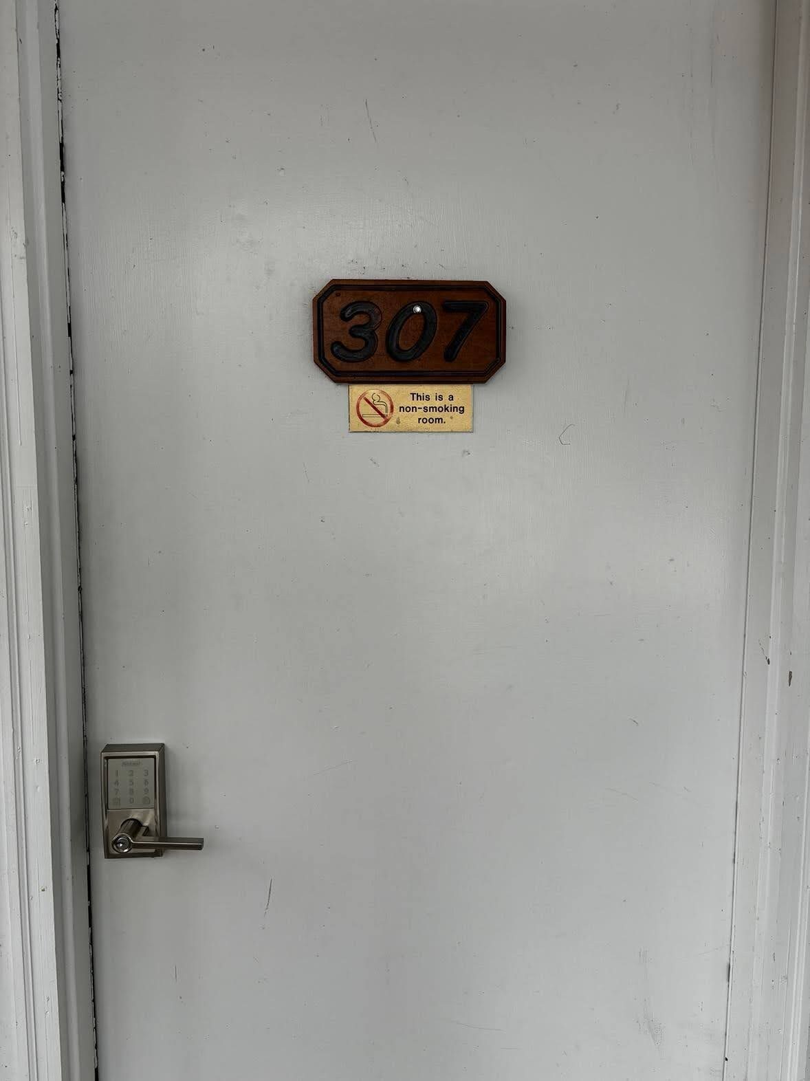Une porte avec une plaque portant le numéro « 307 » et un panneau indiquant qu’il est interdit de fumer.