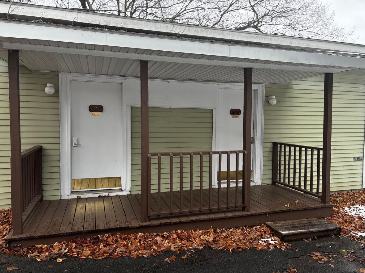 A small, single-story building with a porch, two doors, and a small front yard.