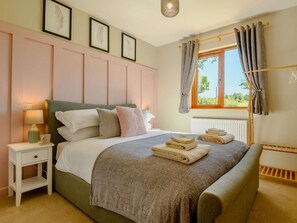 Quarto com cama, mesa de cabeceira, luminária e janela com cortinas.