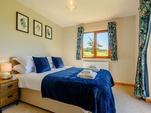 Ein Schlafzimmer mit Bett, Nachttisch, Lampe und einem Fenster mit Vorhängen.