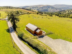 Eine Luftaufnahme eines ländlichen Anwesens mit einem einzelnen Gebäude, einem eingezäunten Feld mit weidenden Tieren und sanften Hügeln im Hintergrund.