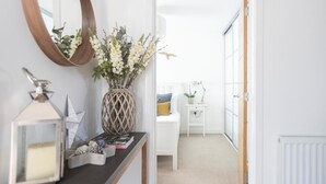 Een hal met een spiegel, een vaas met bloemen, een bureau met boeken en een bed met kussens.