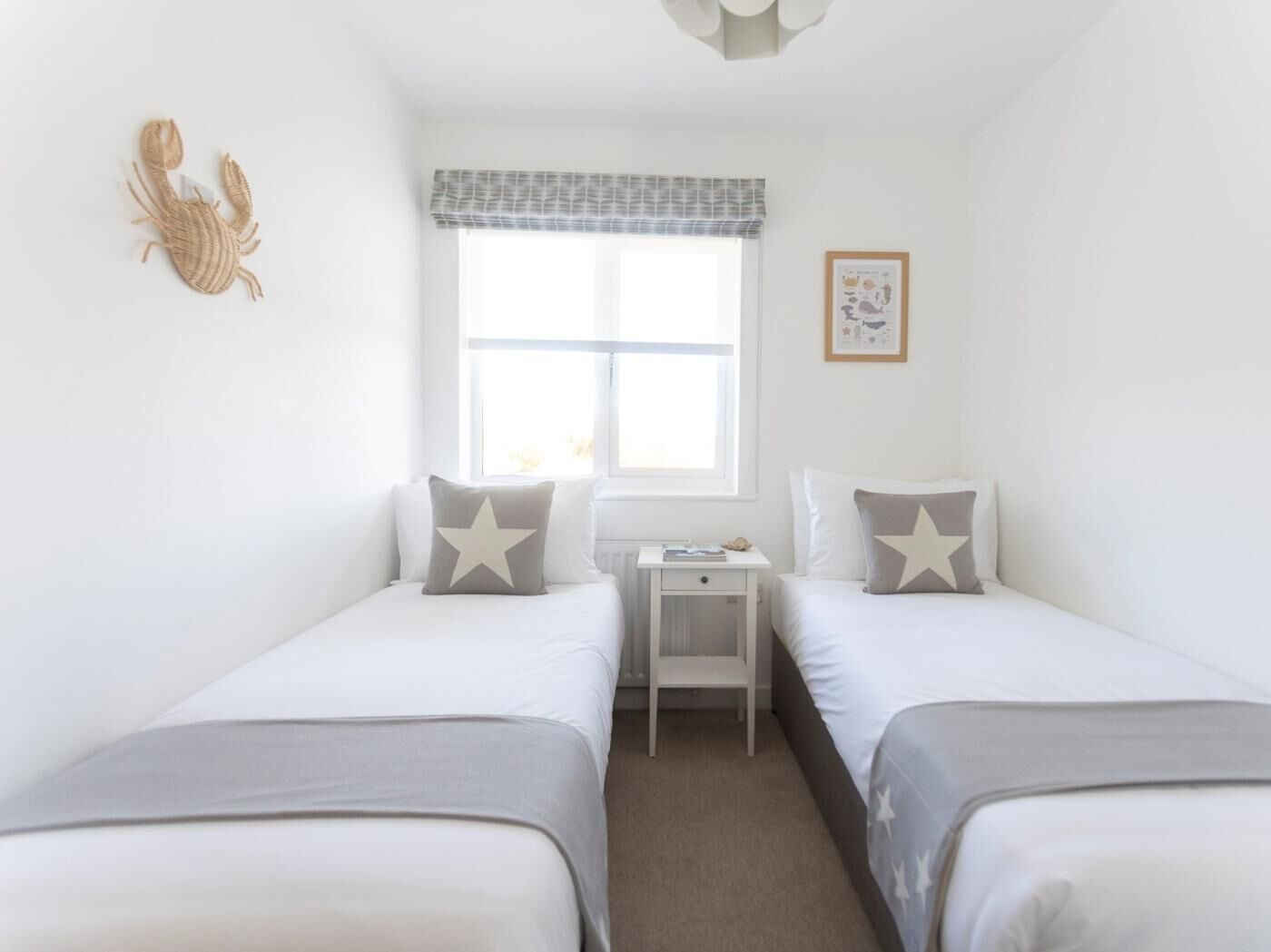A bedroom with two beds, a small bedside table, a window with a view, and a wall decoration.