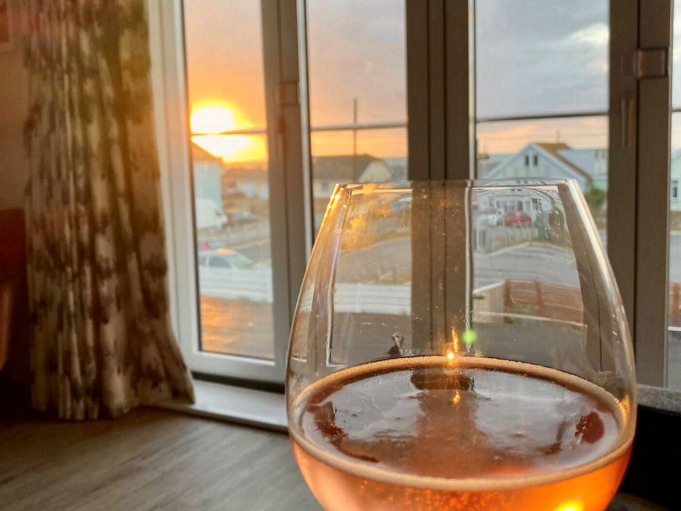 Um copo com líquido âmbar numa janela com vista para um pôr do sol e edifícios.