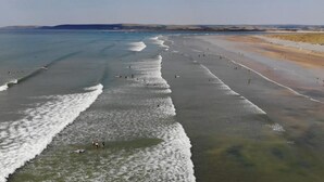 Een strand met golven, mensen en een verre kustlijn.