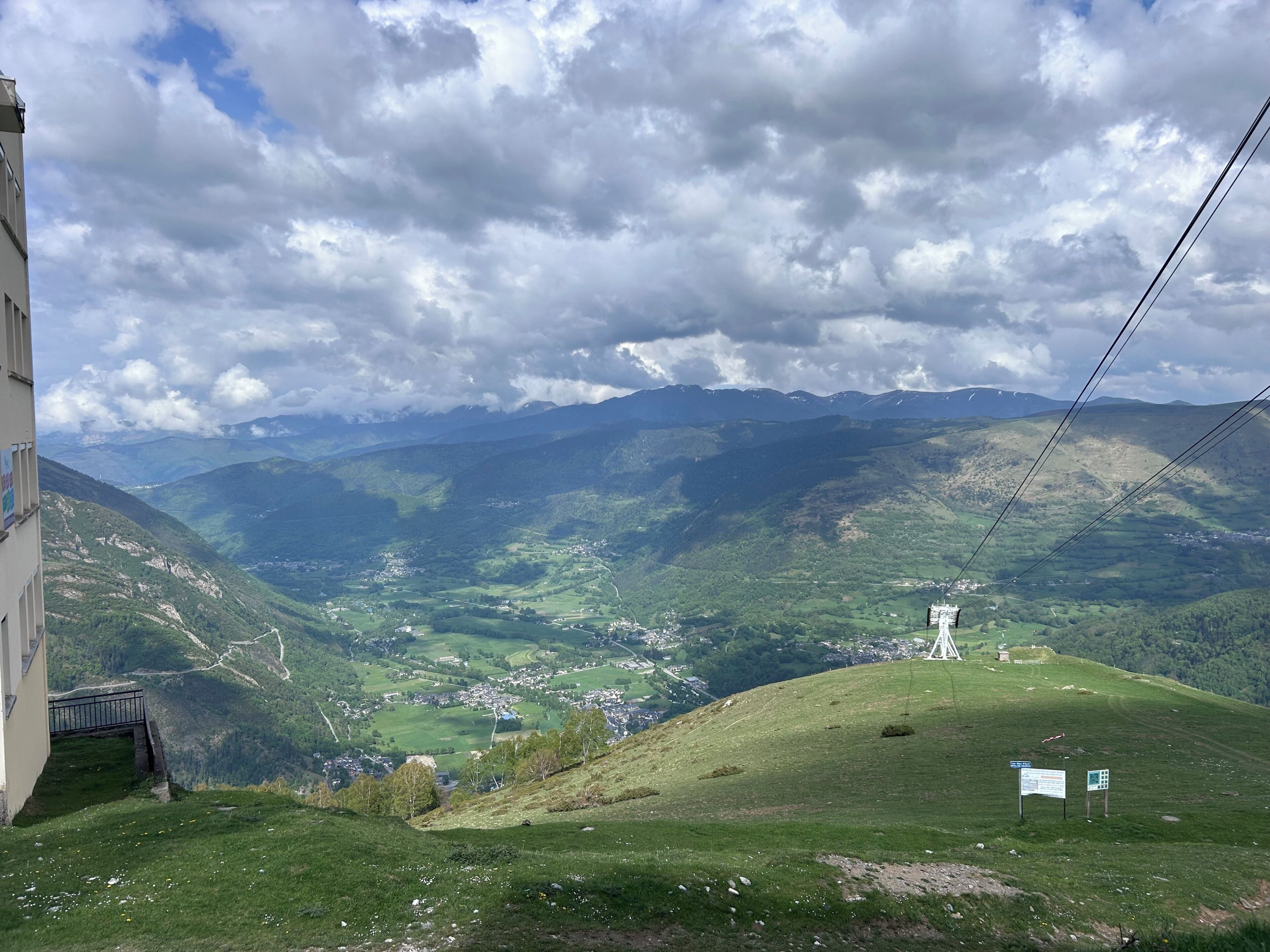 Eine gebirgige Landschaft mit einem Dorf, einem Turm und einem Gebäude mit Balkon.