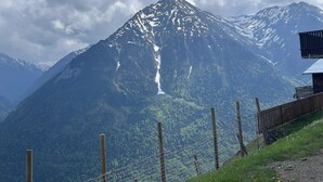 Une montagne dont le sommet est enneigé, une clôture en bois et un bâtiment doté d’un toit en pente.
