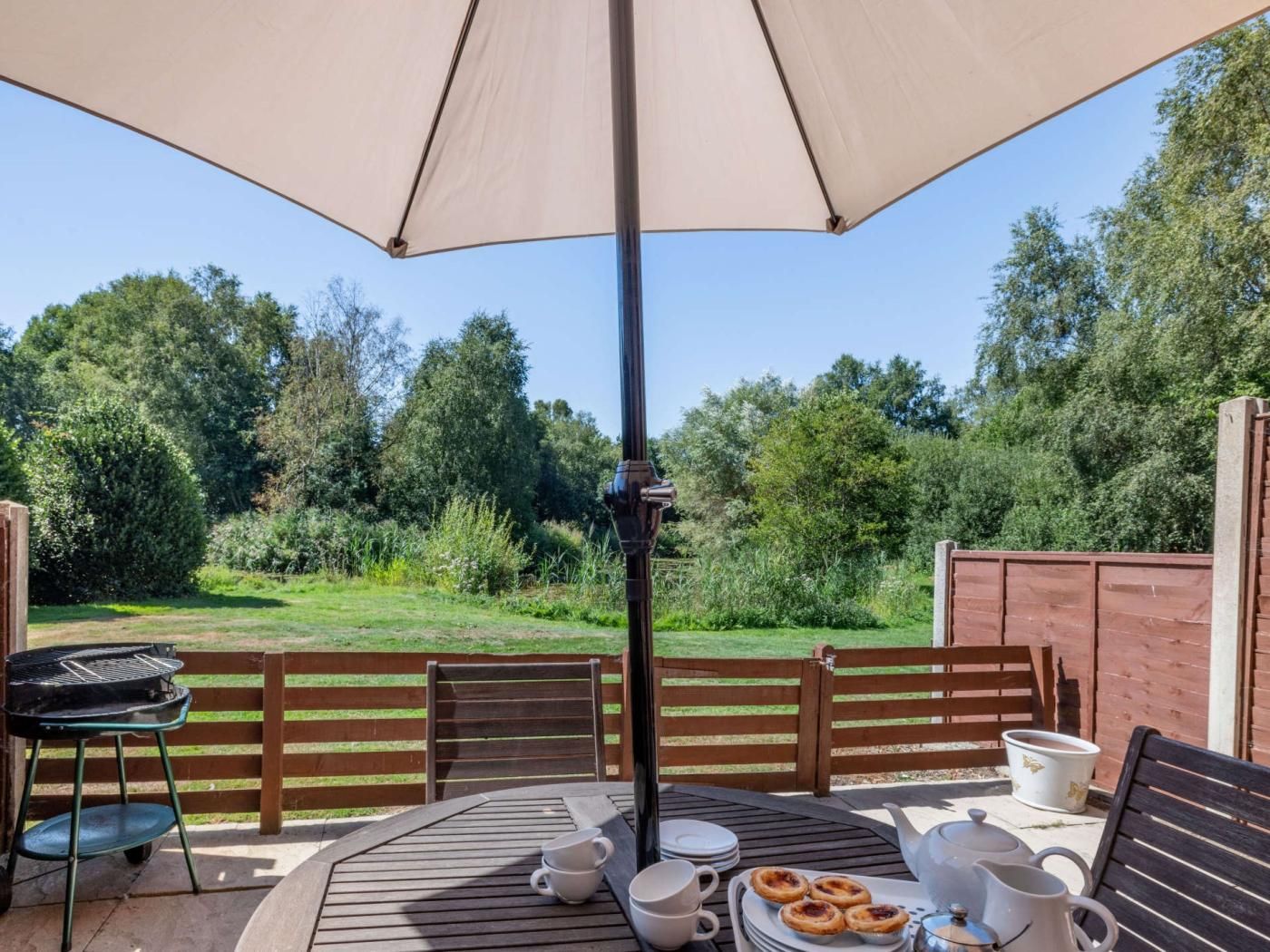 Eine Terrasse im Freien mit Tisch, Stühlen, Grill und einem großen Sonnenschirm, der Schatten spendet.