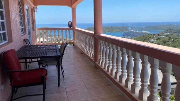 A balcony with a view of the sea, a table with chairs, and a railing.