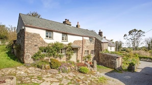 A stone house with a sloped roof, a front door, and a small garden with a gravel path. - 2 Bed in Okehampton (oc-89119) (Throwleigh)