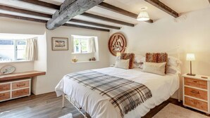 A bedroom with a large bed, wooden beams, a window with curtains, a wall clock, and a bedside table with a lamp. - 2 Bed in Okehampton (oc-89119) (Throwleigh)