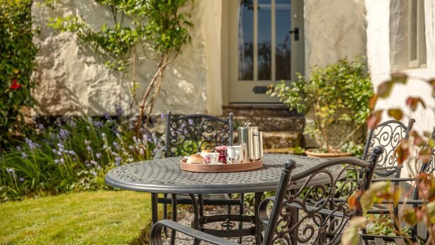A round metal table with chairs, a tray with cups and a thermos, and a stone wall with a door in the background. - 2 Bed in Okehampton (oc-89119) (Throwleigh)