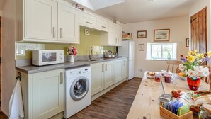 A kitchen with a washing machine, microwave, and a dining area with a table set for a meal. - 2 Bed in Okehampton (oc-89119) (Throwleigh)