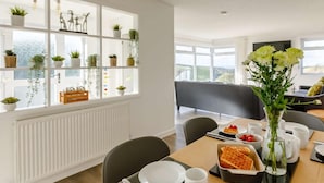 Ett modernt matområde med ett bord dukat för frukost, utsikt över omgivningen och en hylla med växter.