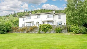 Une maison blanche à deux étages, dotée d’un mur en pierre et d’une pelouse verdoyante.