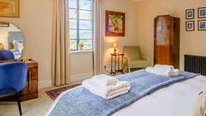 Une chambre d’hôtel avec un lit, une chaise, un bureau, une lampe, un radiateur et une fenêtre avec des rideaux.