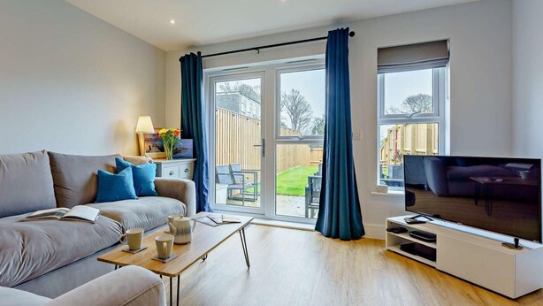 A modern living room with a sofa, coffee table, TV, and a sliding glass door leading to a patio. - 2 Bed in Sandown (oc-89291) (Sandown)