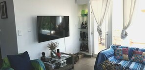 Ein Wohnzimmer mit einem an der Wand befestigten Flachbildfernseher, einer Couch mit gemusterten Kissen, einem Couchtisch mit Dekorationen und einem Bücherregal mit verschiedenen Gegenständen.