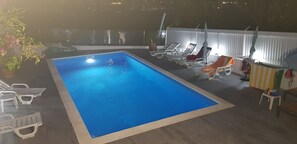 Ein Schwimmbecken mit Liegestühlen und Sonnenschirmen, umgeben von einer Brüstung und Topfpflanzen.