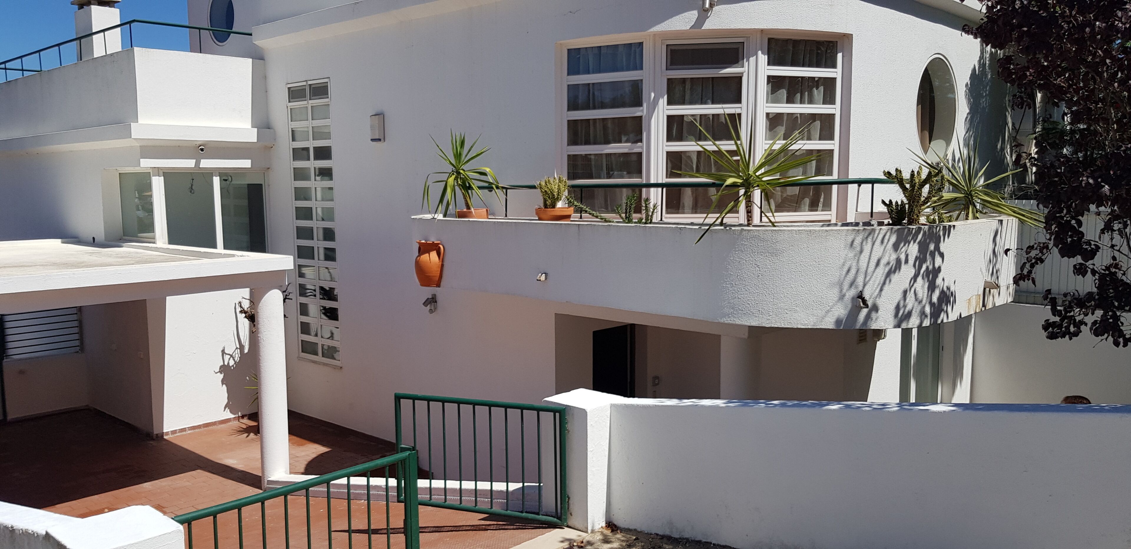 Un edificio blanco con balcón, plantas en macetas y una verja verde.