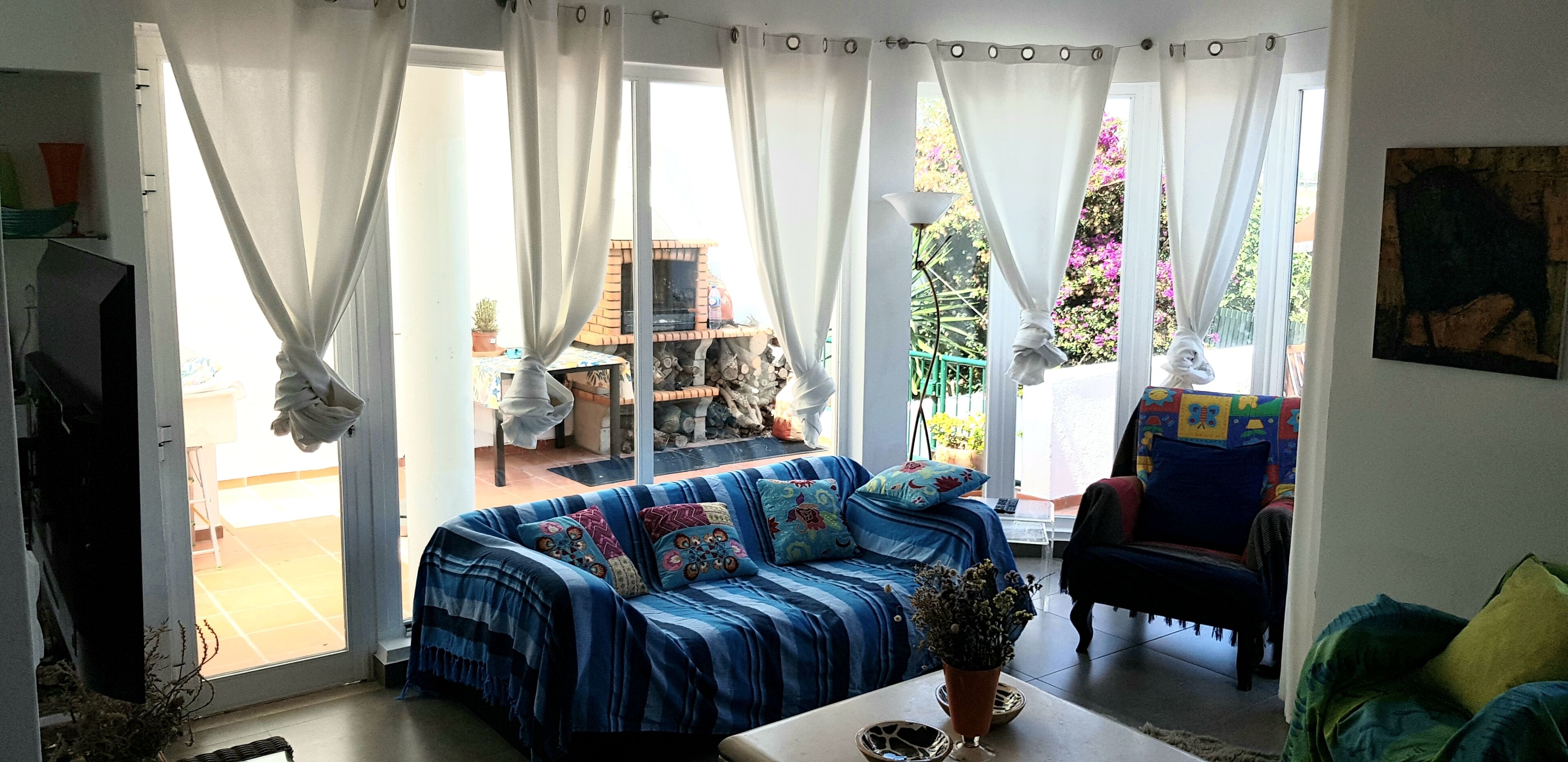 A living room with a blue sofa, a coffee table, and a view of a garden through large windows.