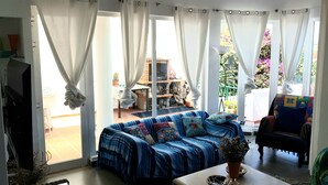 Een woonkamer met een blauwe bank, een bijzettafeltje en uitzicht op een tuin door grote ramen.