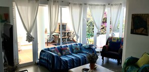 Ein Wohnzimmer mit einem blauen Sofa, einem Couchtisch und Blick auf einen Garten durch große Fenster.
