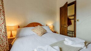 Ein ordentlich bezogenes Bett mit weißen Leinentüchern und einem Zierkissen, ein Holzkopfende, Nachttischlampen und eine Holztür mit einem Spiegel.