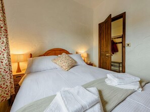 Ein ordentlich bezogenes Bett mit weißen Leinentüchern und einem Zierkissen, ein Holzkopfende, Nachttischlampen und eine Holztür mit einem Spiegel.