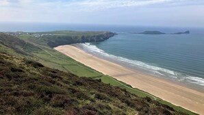 Eine Küstenlandschaft mit Strand, grünen Hügeln und einer fernen Insel.