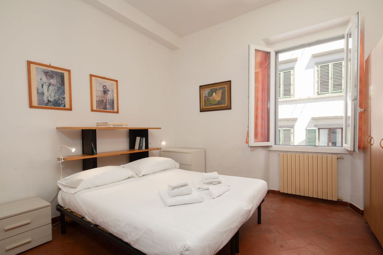 Un dormitorio con cama, mesitas de noche, una ventana con contraventanas y una obra de arte colgada en la pared.