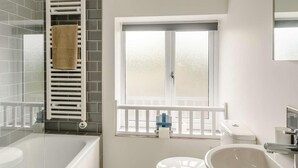 A bathroom with a bathtub, a toilet, a sink, a window with a view, and a towel rack. - 2 Bed in Cardigan (oc-89315) (Tresaith)