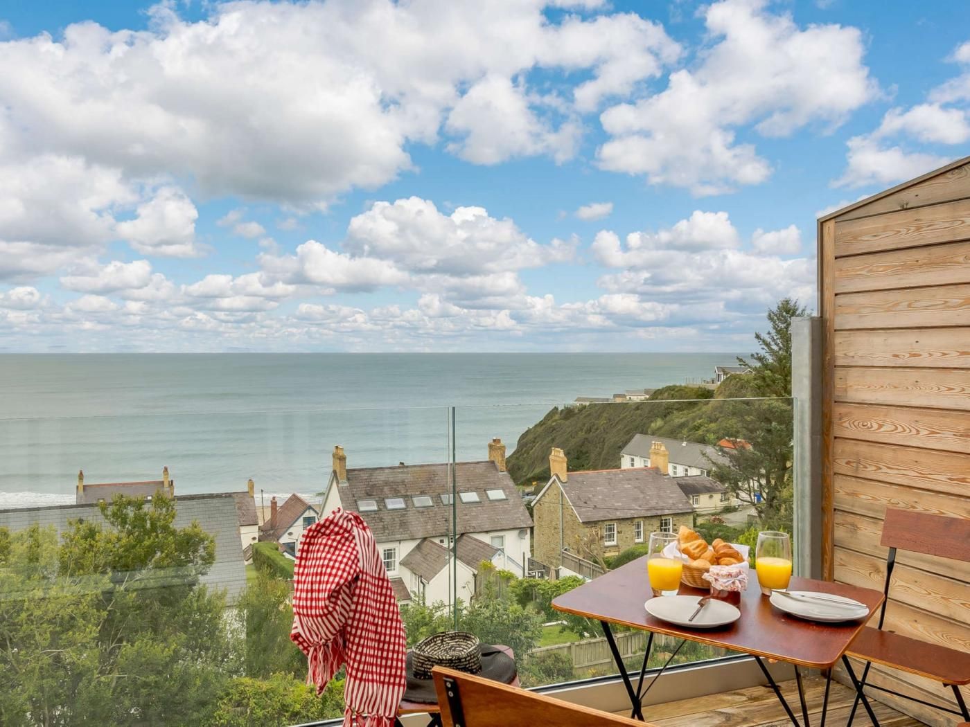 A balcony with a table set for breakfast overlooking a coastal view.