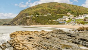 A coastal landscape with a hill, rocky shoreline, and a row of houses. - 2 Bed in Cardigan (oc-89315) (Tresaith)