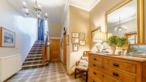 A hallway with a staircase, a wooden dresser, a mirror, and a chandelier. - 5 Bed in Melrose (oc-89348) (Newtown Saint Boswells)
