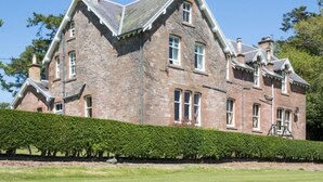 A large, stone building with multiple windows and a well-maintained hedge in front. - 5 Bed in Melrose (oc-89348) (Newtown Saint Boswells)
